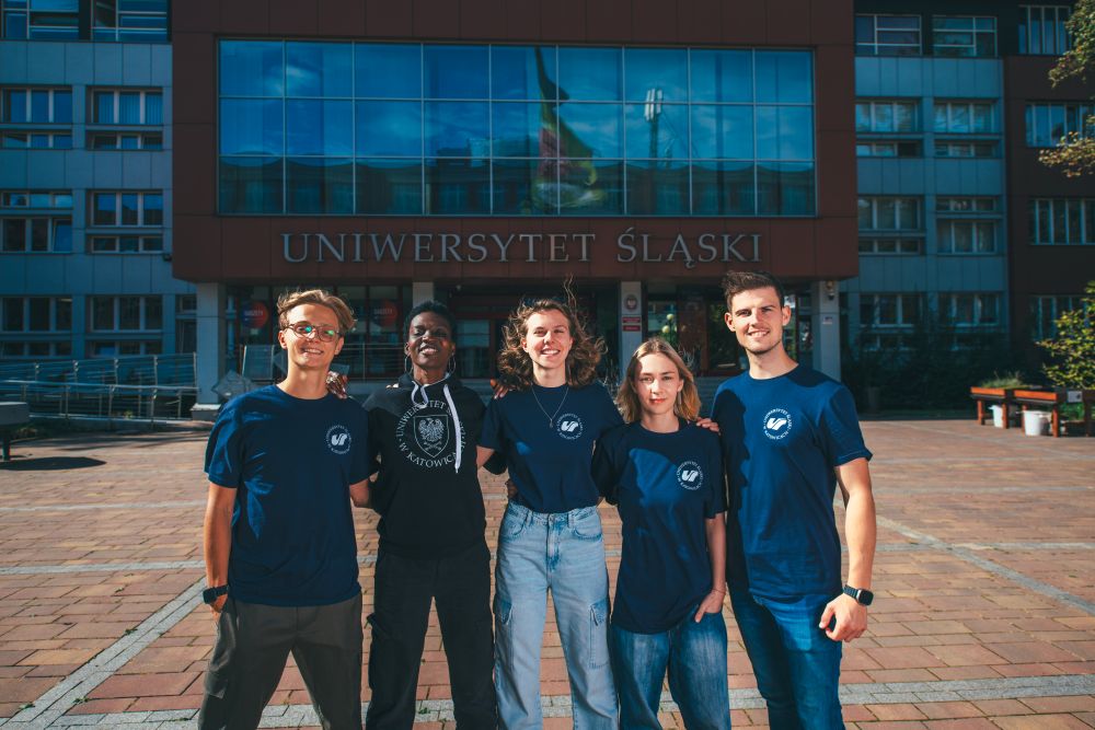 Pięcioro studentów, trzymajacych się za barki, przed budynkiem Rektoratu