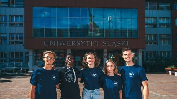 Pięcioro studentów, trzymajacych się za barki, przed budynkiem Rektoratu