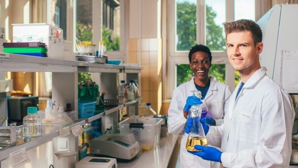 Dwójka studentów, kobieta i mężczyzna w laboratorium. Mężczyzna trzma menzurkę